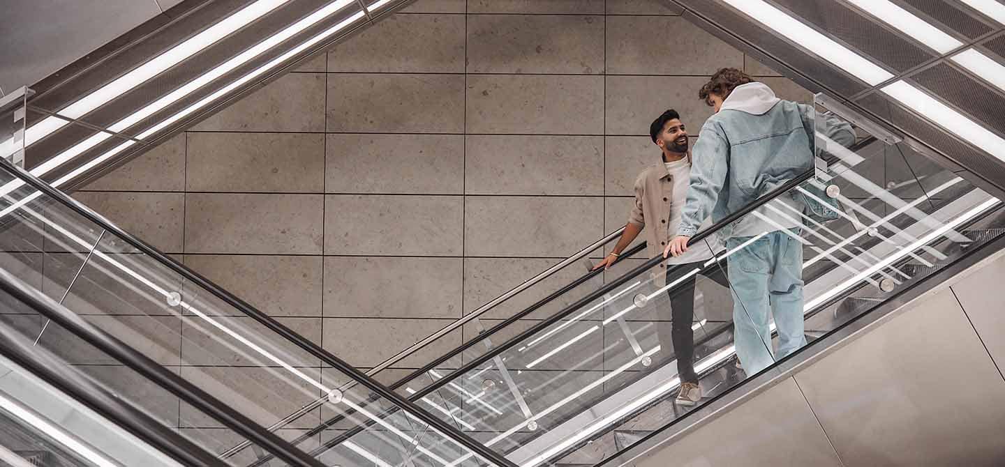 img_two_men_talking_in_escalator_1440x670